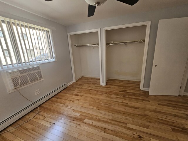 5349 N Delphia Ave Unit 150, Chicago, IL 60656 - unfurnished bedroom with multiple closets, a baseboard radiator, hardwood / wood-style floors, a ceiling fan, and an AC wall unit