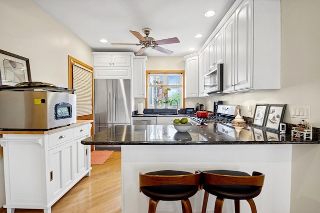 5055 N California Ave Unit 1S, Chicago, IL 60625 - kitchen featuring appliances with stainless steel finishes, a peninsula, dark stone countertops, recessed lighting, and white cabinetry