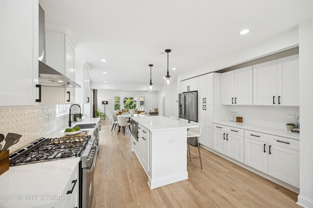 920 Hayes Ave, Oak Park, IL 60302 - kitchen with appliances with stainless steel finishes, wall chimney range hood, light wood-type flooring, white cabinetry, and a breakfast bar area