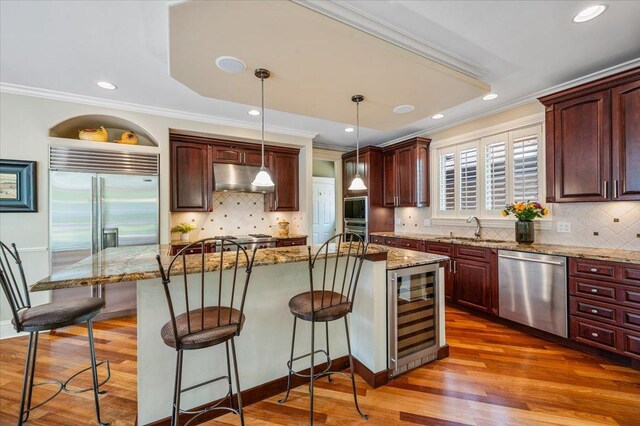 320 Vista Dr, Wilmette, IL 60091 - kitchen with beverage cooler, built in appliances, under cabinet range hood, wood finished floors, and crown molding