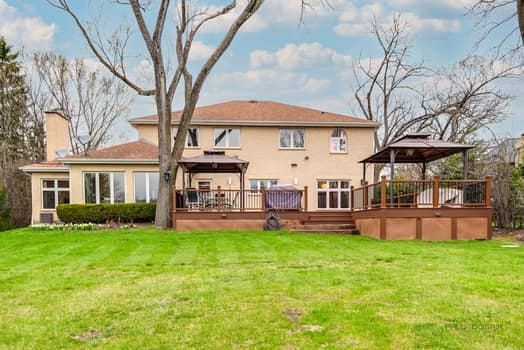 rear view of property featuring a gazebo, a chimney, a wooden deck, and a yard