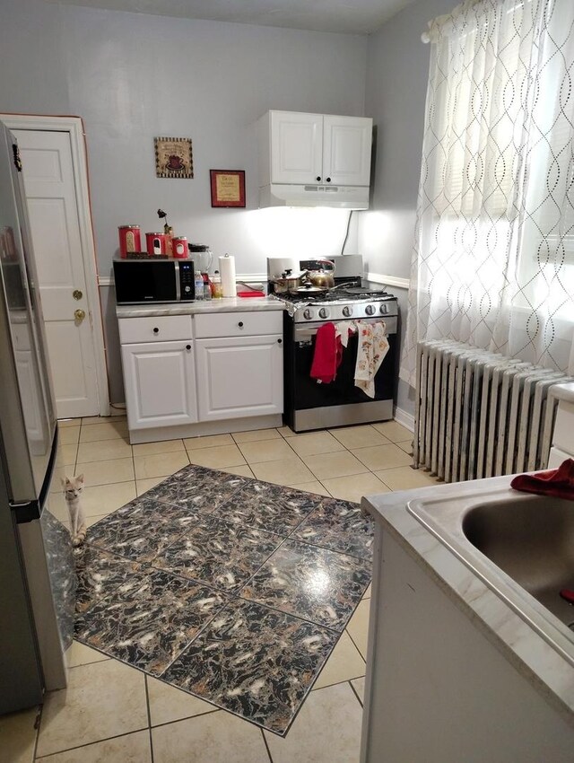 2240 W 50th Pl, Chicago, IL 60609 - kitchen with radiator heating unit, appliances with stainless steel finishes, white cabinetry, under cabinet range hood, and light tile patterned flooring