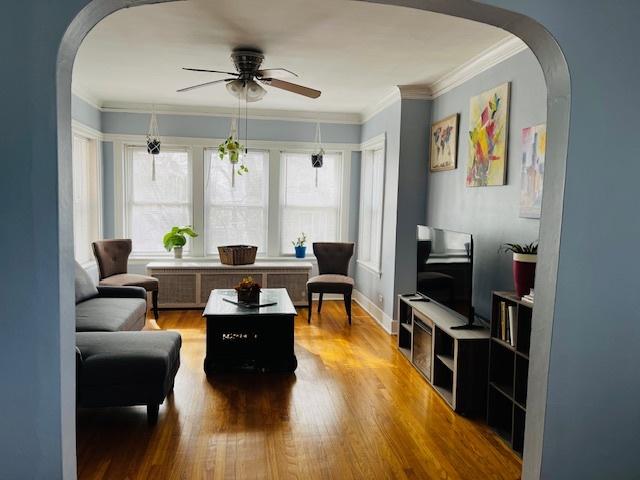 living room featuring ceiling fan, arched walkways, wood finished floors, crown molding, and radiator