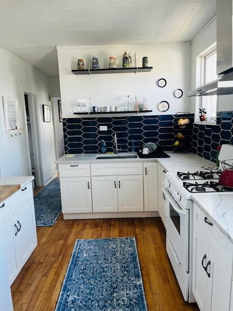 kitchen with white gas stove, dark wood-style floors, white cabinetry, and decorative backsplash