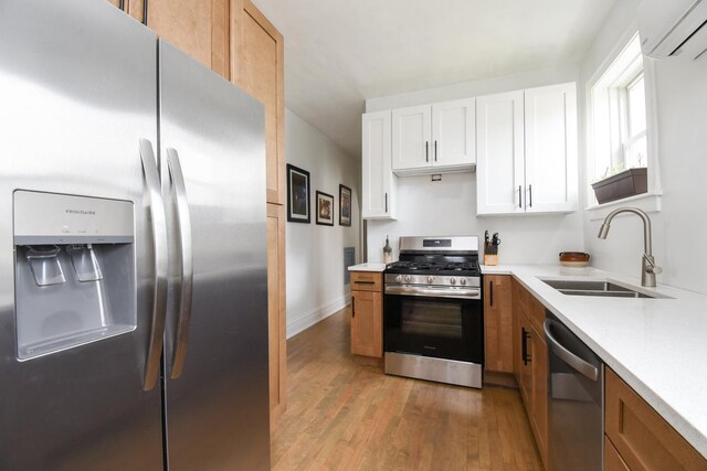 kitchen featuring stainless steel appliances, light wood-type flooring, light countertops, a wall mounted air conditioner, and white cabinetry