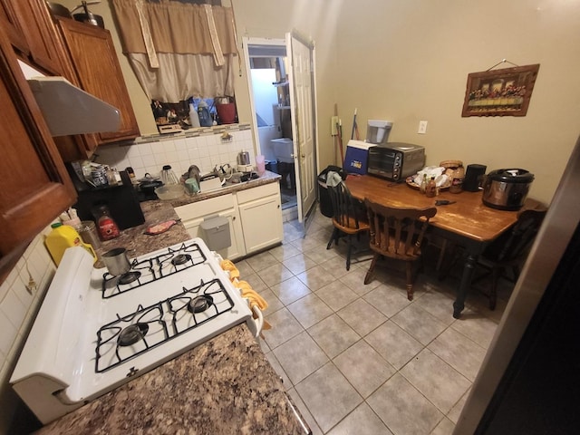 817 N Kolin Ave, Chicago, IL 60651 - kitchen with range, under cabinet range hood, light tile patterned floors, brown cabinets, and decorative backsplash
