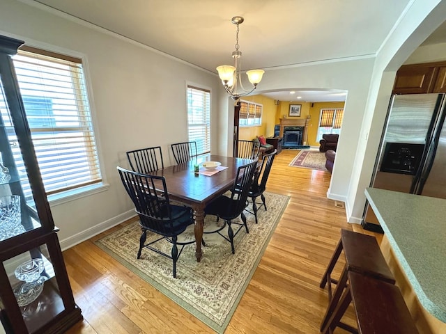 10043 S Artesian Ave, Chicago, IL 60655 - dining space featuring crown molding, light wood-style floors, a fireplace with raised hearth, a chandelier, and arched walkways