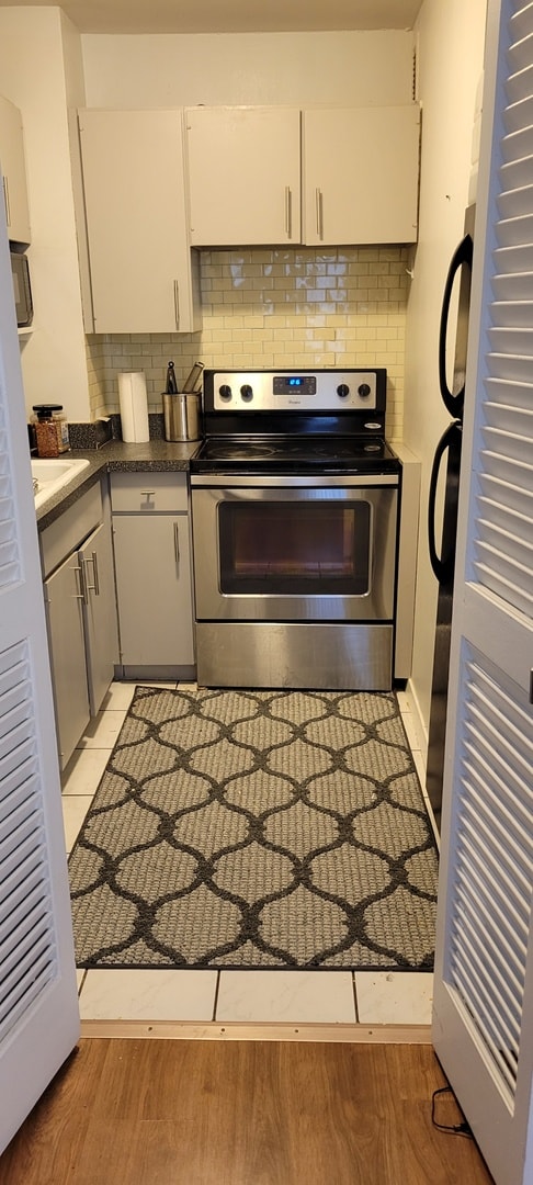 21 W Goethe St Unit 7C, Chicago, IL 60610 - kitchen featuring stainless steel electric range oven, backsplash, white cabinetry, and light wood-style floors