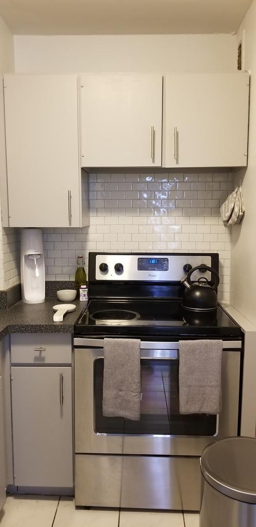 21 W Goethe St Unit 7C, Chicago, IL 60610 - kitchen featuring stainless steel electric range oven, white cabinetry, backsplash, light tile patterned floors, and dark countertops