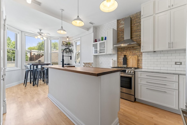1128 W Wolfram St Unit 2, Chicago, IL 60657 - kitchen with wall chimney range hood, stainless steel gas stove, butcher block countertops, backsplash, and a center island with sink