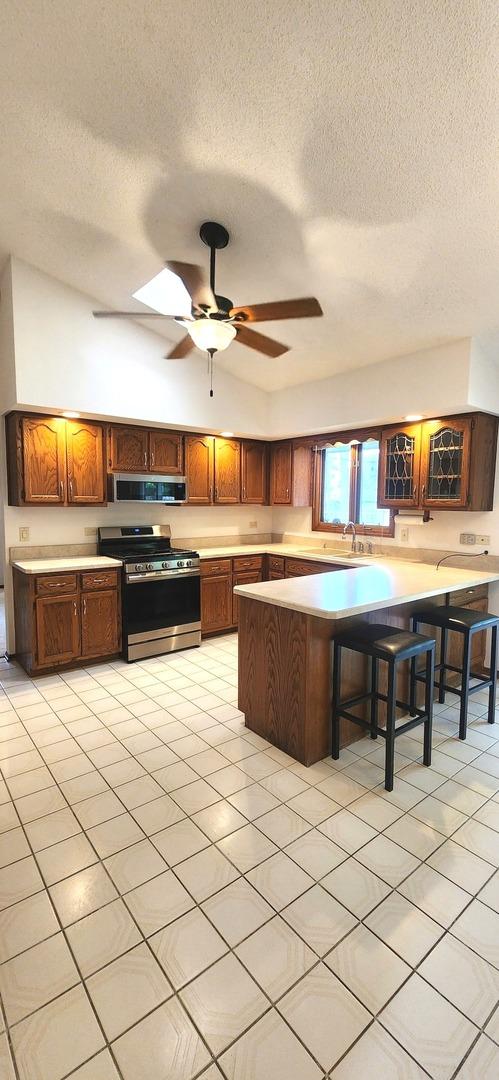 18068 Jason Ln, Lansing, IL 60438 - kitchen with appliances with stainless steel finishes, a peninsula, a textured ceiling, a ceiling fan, and a kitchen breakfast bar