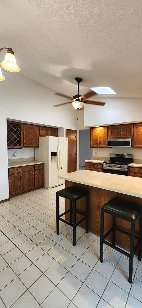 18068 Jason Ln, Lansing, IL 60438 - kitchen featuring stainless steel stove, range hood, white fridge with ice dispenser, light countertops, and a kitchen bar
