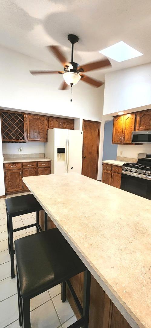 18068 Jason Ln, Lansing, IL 60438 - kitchen featuring appliances with stainless steel finishes, a kitchen bar, light countertops, brown cabinetry, and ceiling fan