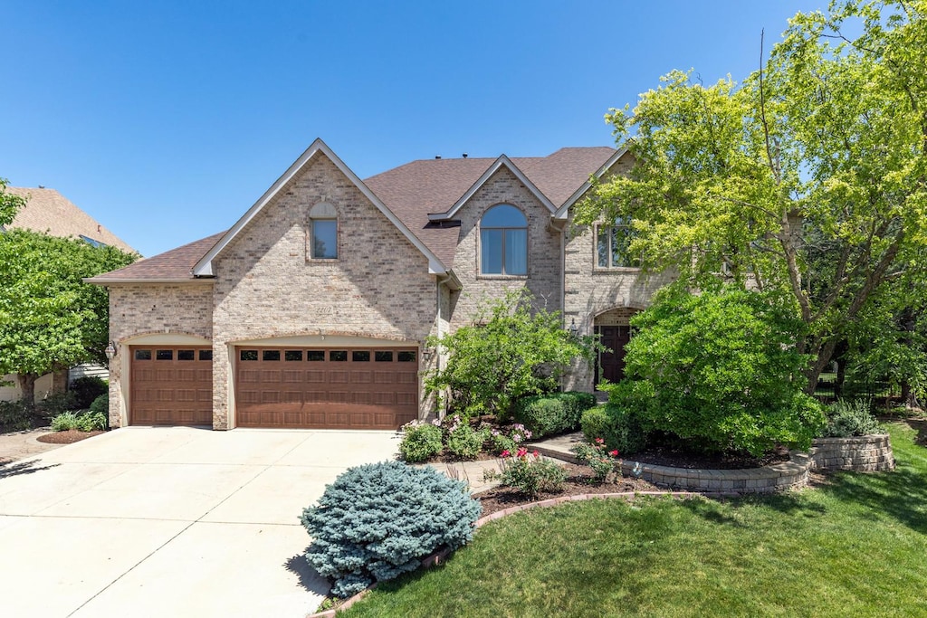 2207 Stowe Cir, Naperville, IL 60564 - traditional-style house featuring driveway, a garage, roof with shingles, brick siding, and a front yard