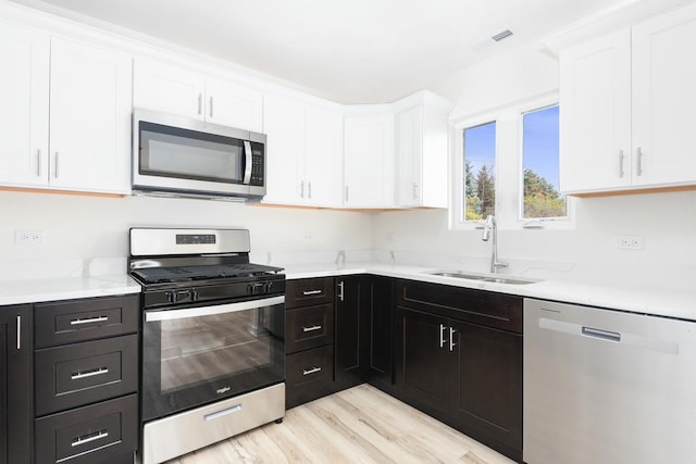 5540 Hearthside Dr, Bourbonnais, IL 60914 - kitchen with stainless steel appliances, a sink, white cabinetry, dark cabinetry, and light wood finished floors