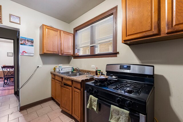 8122 S Evans Ave, Chicago, IL 60619 - kitchen with black gas range oven, a sink, baseboards, light tile patterned floors, and brown cabinetry