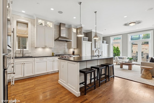 1230 W Cornelia Ave, Chicago, IL 60657 - kitchen featuring wall chimney range hood, dark countertops, a kitchen breakfast bar, light wood-style flooring, and crown molding
