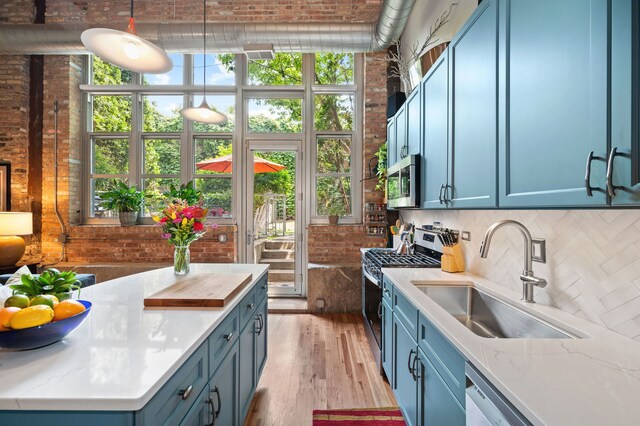 2111 W Churchill St Unit 112, Chicago, IL 60647 - kitchen with stainless steel appliances, backsplash, brick wall, light wood finished floors, and pendant lighting