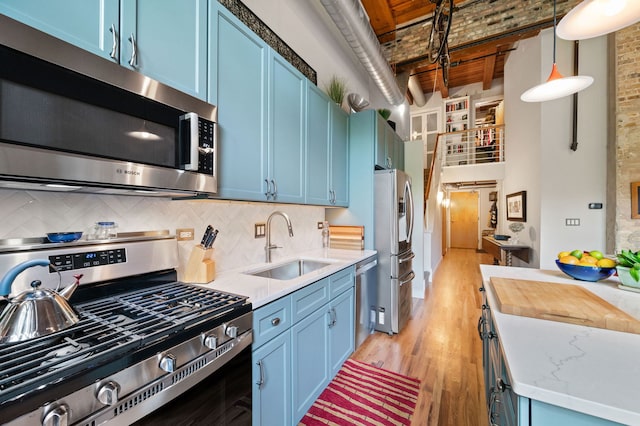 2111 W Churchill St Unit 112, Chicago, IL 60647 - kitchen with appliances with stainless steel finishes, blue cabinetry, backsplash, a towering ceiling, and decorative light fixtures