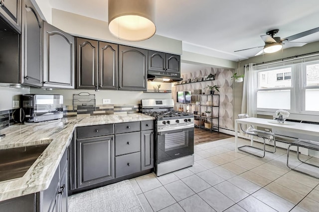 6468 N NW Hwy Unit A1, Chicago, IL 60631 - kitchen featuring stainless steel range with gas stovetop, under cabinet range hood, ceiling fan, light tile patterned flooring, and light stone countertops