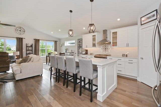 1104 Hershey Rd, Normal, IL 61761 - kitchen featuring wall chimney range hood, open floor plan, lofted ceiling, light wood-type flooring, and a breakfast bar