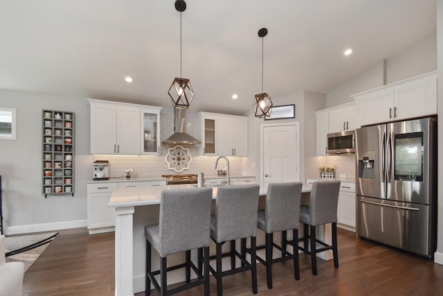 1104 Hershey Rd, Normal, IL 61761 - kitchen featuring appliances with stainless steel finishes, wall chimney range hood, backsplash, white cabinets, and a kitchen island with sink