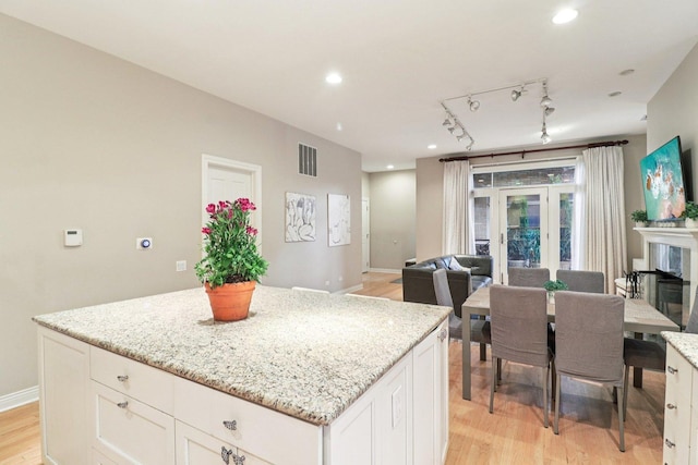 1347 W Washington Blvd Unit 2D, Chicago, IL 60607 - kitchen featuring light wood-style floors, a kitchen island, white cabinetry, light stone counters, and rail lighting