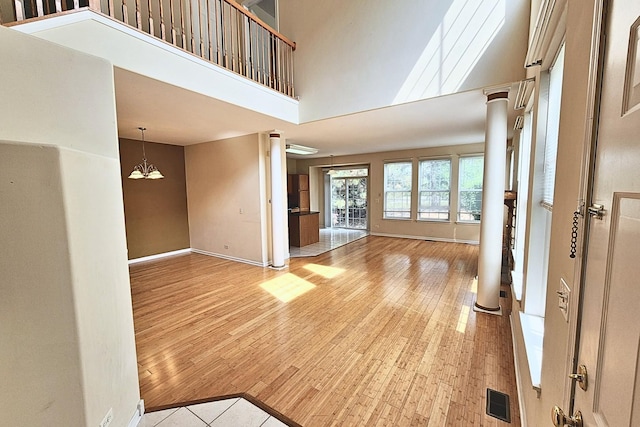 6 Clara Ct, Algonquin, IL 60102 - unfurnished living room featuring light wood-style floors, ornate columns, baseboards, a towering ceiling, and a chandelier