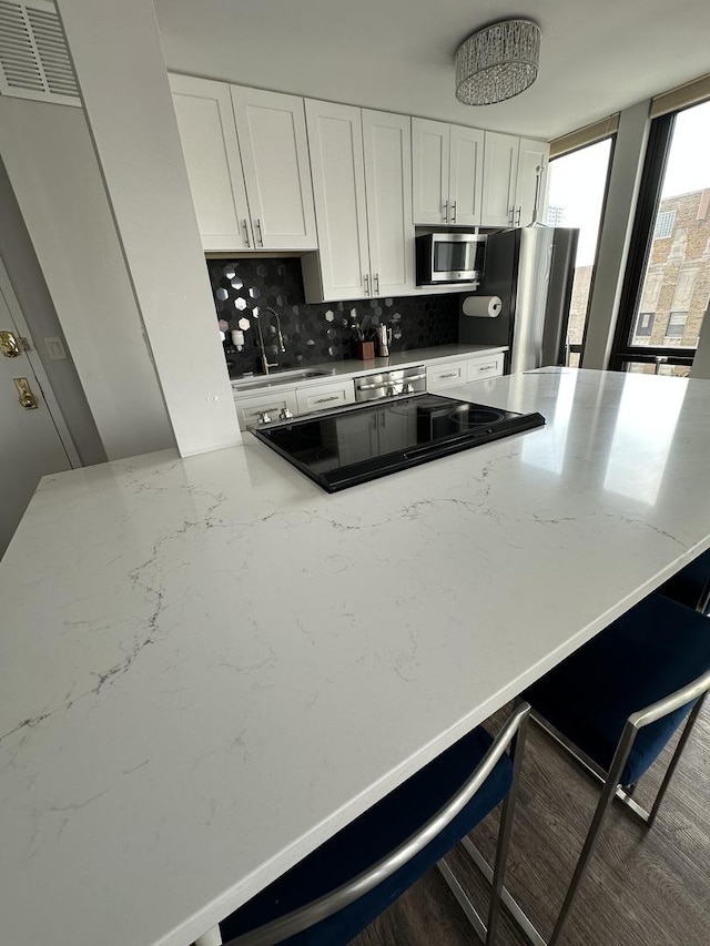1 E Scott St Unit 1910, Chicago, IL 60610 - kitchen with appliances with stainless steel finishes, decorative backsplash, white cabinetry, light stone countertops, and a kitchen bar
