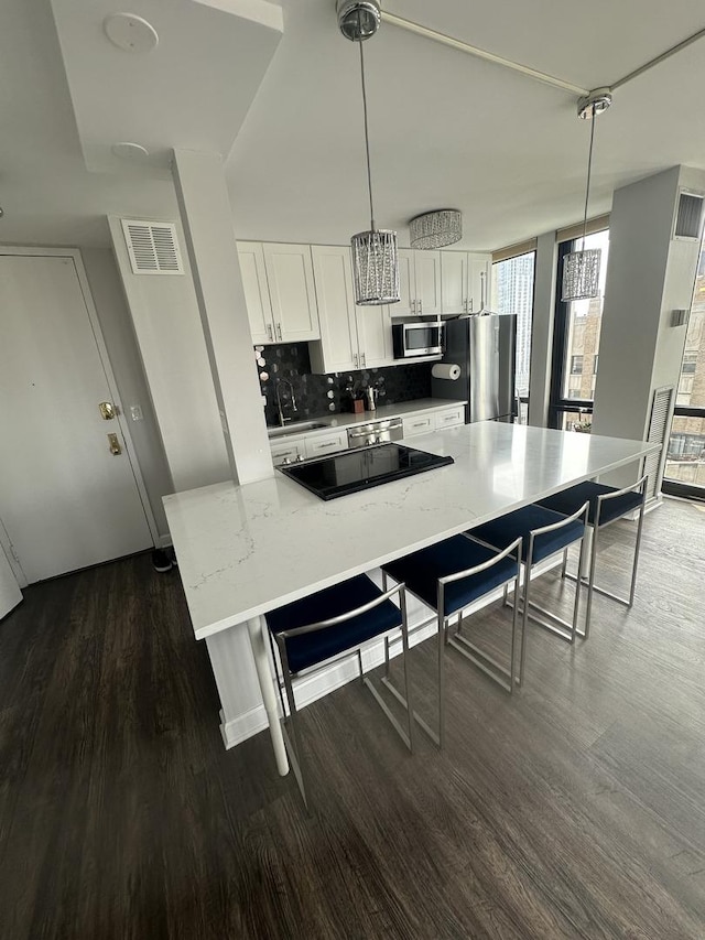 1 E Scott St Unit 1910, Chicago, IL 60610 - kitchen with appliances with stainless steel finishes, dark wood-style floors, white cabinets, a kitchen bar, and light stone counters