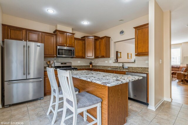 6812 Meadow Ln, Morton Grove, IL 60053 - kitchen featuring appliances with stainless steel finishes, tasteful backsplash, a breakfast bar, light stone counters, and brown cabinetry