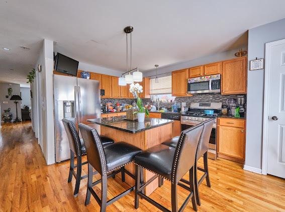 4813 W 23rd St, Cicero, IL 60804 - kitchen featuring appliances with stainless steel finishes, light wood finished floors, decorative backsplash, and decorative light fixtures