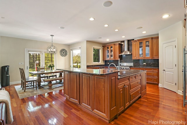 1400 Banbury Rd, Inverness, IL 60067 - kitchen featuring wall chimney range hood, brown cabinetry, dark wood-style flooring, a chandelier, and a kitchen island with sink