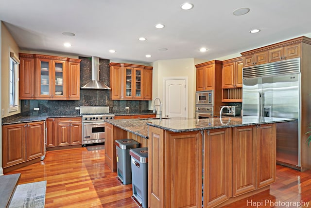 1400 Banbury Rd, Inverness, IL 60067 - kitchen with built in appliances, wall chimney exhaust hood, brown cabinetry, a kitchen island with sink, and recessed lighting