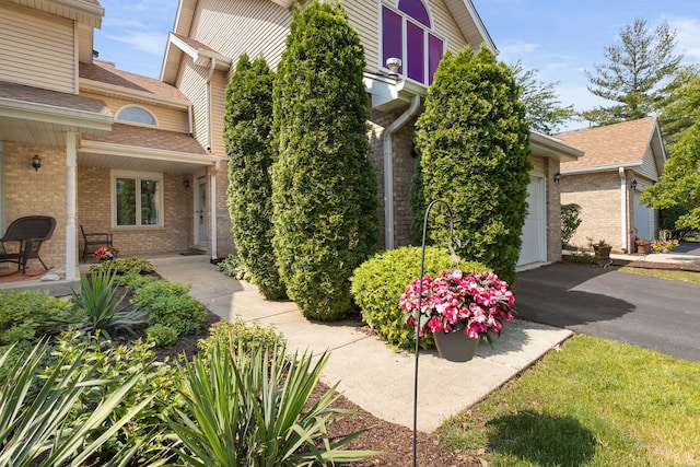 view of property exterior featuring driveway, brick siding, and roof with shingles
