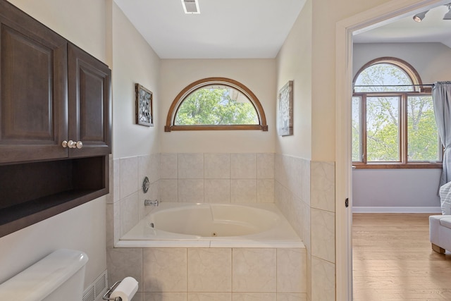 bathroom with a garden tub, plenty of natural light, and wood finished floors