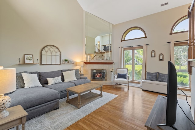 living area featuring a towering ceiling, wood finished floors, plenty of natural light, and a tiled fireplace