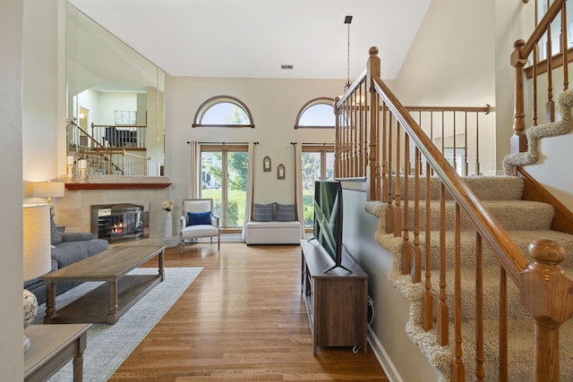 living room featuring wood finished floors, stairway, a towering ceiling, and a tile fireplace