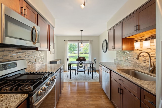 kitchen with stainless steel appliances, light wood-style floors, tasteful backsplash, light stone counters, and hanging light fixtures