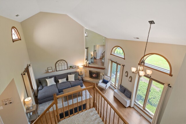 living room featuring high vaulted ceiling, a tile fireplace, healthy amount of natural light, wood finished floors, and a chandelier