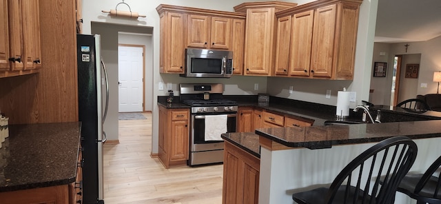 6638 Key Largo Dr, Machesney Park, IL 61103 - kitchen with stainless steel appliances, light wood-type flooring, a peninsula, a kitchen bar, and dark stone countertops