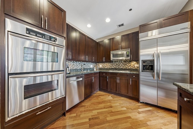 333 N Canal St Unit 2505, Chicago, IL 60606 - kitchen featuring appliances with stainless steel finishes, light wood-style flooring, dark stone counters, dark brown cabinetry, and backsplash