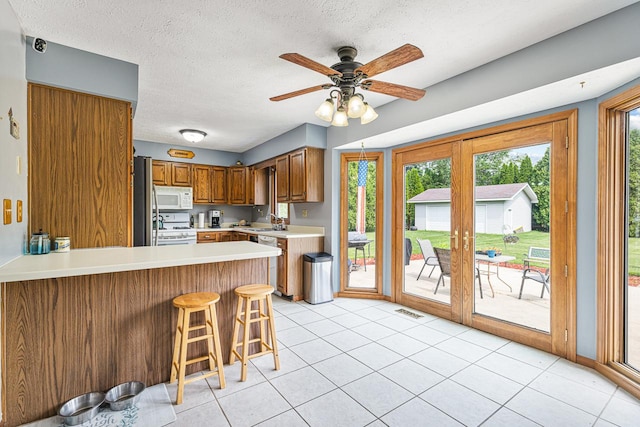 9650 Edgefield Rd, Roscoe, IL 61073 - kitchen with white appliances, a peninsula, brown cabinetry, light countertops, and a sink