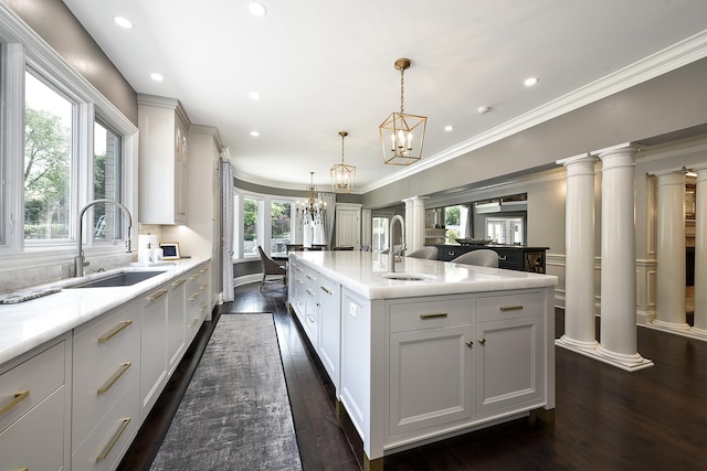 1877 Banbury Rd, Inverness, IL 60067 - kitchen featuring dark wood-style floors, light countertops, a kitchen island with sink, decorative columns, and a chandelier