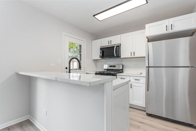 7490 Filmore Ave, Hanover Park, IL 60133 - kitchen featuring appliances with stainless steel finishes, white cabinets, light wood-type flooring, backsplash, and a peninsula