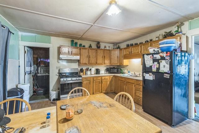 420 N 9th St, Herrin, IL 62948 - kitchen featuring freestanding refrigerator, stainless steel gas stove, under cabinet range hood, light countertops, and light wood-style flooring