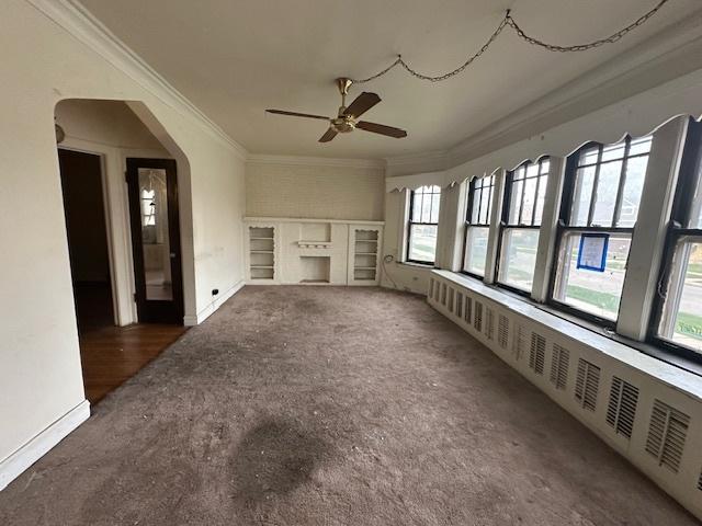unfurnished living room with ornamental molding, a ceiling fan, baseboards, carpet floors, and arched walkways