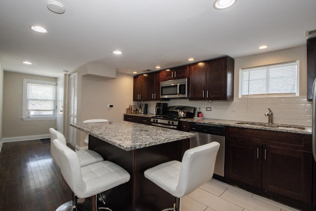 5236 W Nelson St, Chicago, IL 60641 - kitchen featuring appliances with stainless steel finishes, a kitchen bar, a center island, tasteful backsplash, and light stone counters