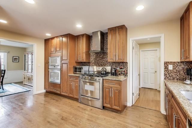 613 Michelline Ln, Northbrook, IL 60062 - kitchen featuring wall chimney range hood, gas range, light wood-type flooring, brown cabinetry, and white microwave