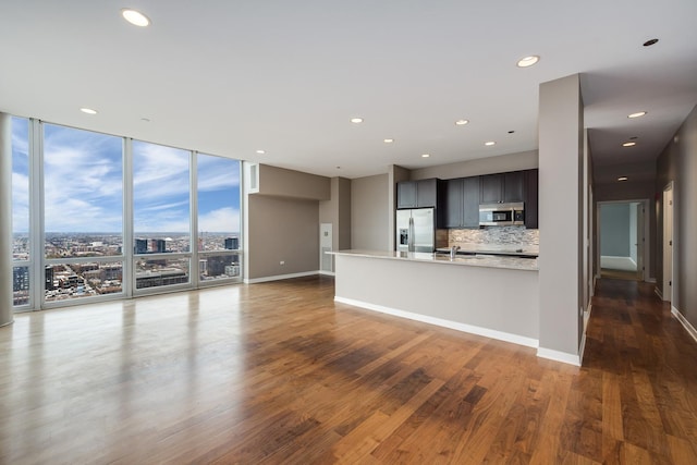 unfurnished living room featuring floor to ceiling windows, dark wood-style flooring, recessed lighting, baseboards, and a sink